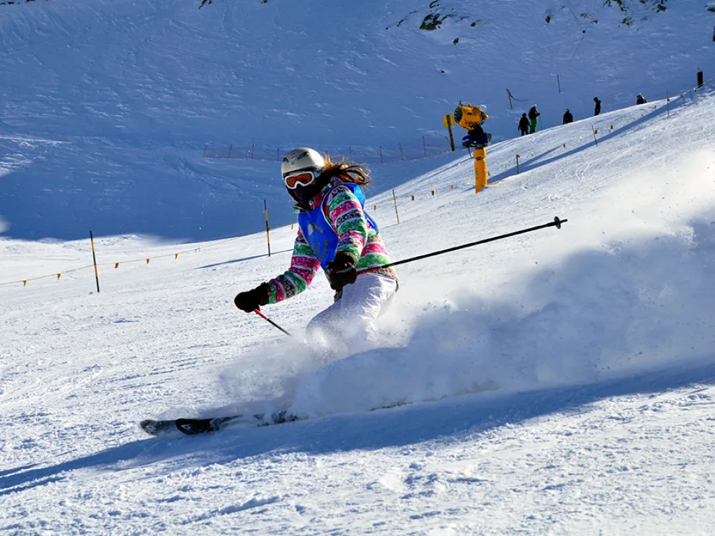 Skifahrerin in bunter Jacke bremst mit Schneefontäne.